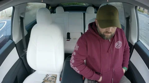 Handsome man getting into car, buckle up and drink coffee in electric car TESLA Stock Footage 237403228