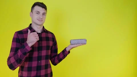 Handsome man with gift box in palm shows like and smiles on yellow background Stock Footage 133485426