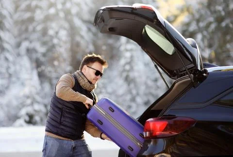 Handsome man going to vacations, loading his suitcase in car trunk Foto stock
