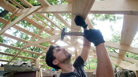 Handsome man hammers a nail into the roof board of his garage Stock Footage