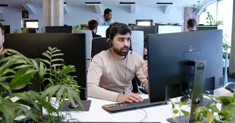 Handsome man in headset sitting at computer screen and talking with client Stock Footage 179984924