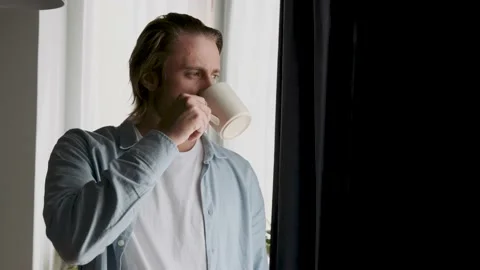 Handsome man in his 30s drinking coffee or tea near the window Stock Footage 195953750