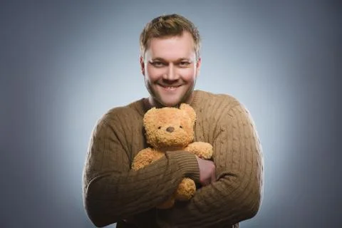 Handsome man is holding a teddy bear and smiling on gray background Stock Photos