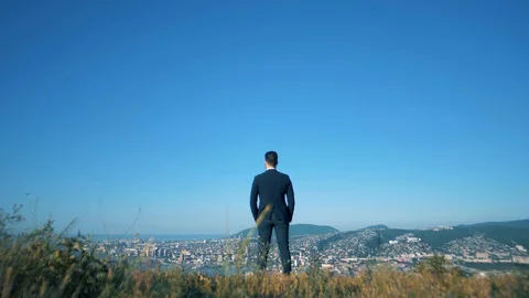 A handsome man in a jacket stands on top of a mountain and looks at his city Video stock 128747978