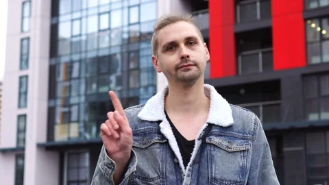 Handsome man in jean jacket standing alone outdoor and saying no by waving his Stock Footage 145484378