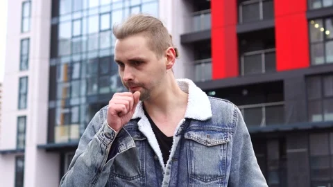 Handsome man in jean jacket standing alone outdoor and sneezes or coughing. Stock Footage 145485646