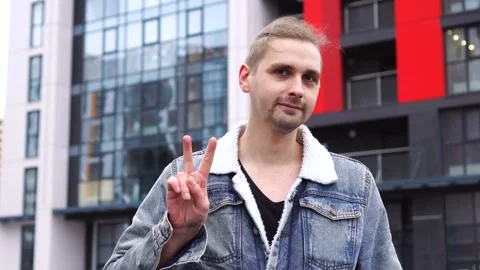 Handsome man in jean jacket standing alone outdoor and showing peace gesture Stock Footage 145486320