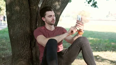 Handsome man leaning on a tree and doing selfies on smartphone Stock-Footage 69963095