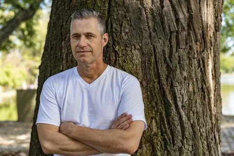 A handsome man leaning on a tree with his arms folded and looking at the ca.. Stock Photos