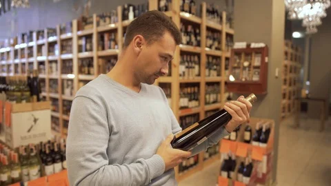 Handsome man learning the label on the wine bottle in a wine shop. Wine bottles Video stock 99384923