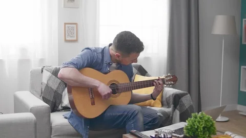 Handsome man learns to play the guitar with the help of an online tutorial Vídeos de archivo 106869628