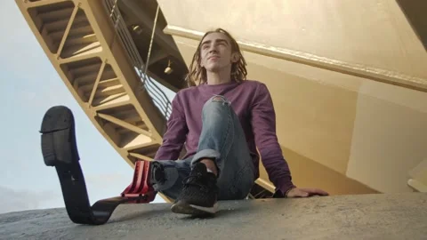 Handsome man with leg prosthesis stands on steps at sunset 库存影片 194602441