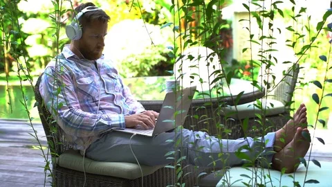 Handsome man listening music while typing on laptop in the garden Stock-Footage 79390091
