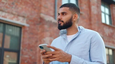 Handsome man looking up after sending text messages on mobile phone outdoors Video stock 250387229