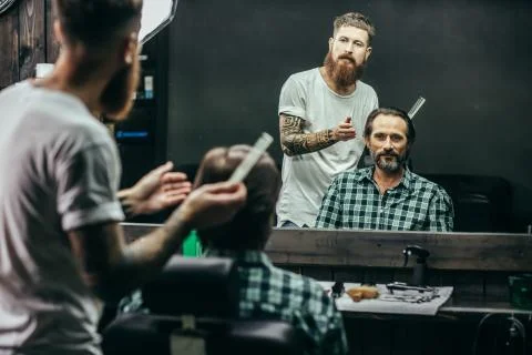 Handsome man looking at his reflection while the barber thinking Stock Photos