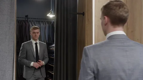 Handsome man looking in mirror while trying on new suit in shop Stock Footage 297471246