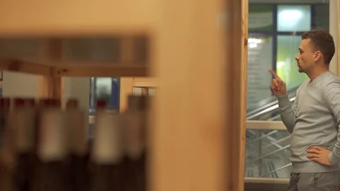 Handsome man looking on the wine bottle on a wooden shelf in liquor store Stock Footage 99386230