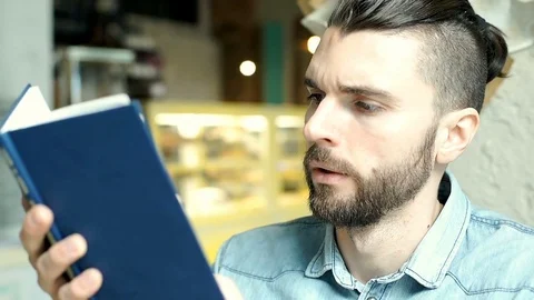 Handsome man looks bored while reading book in the cafe Stock-Footage 73186148