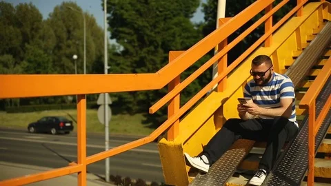 Handsome man looks happy while texting on smartphone next to the highway Stock Footage 76979793