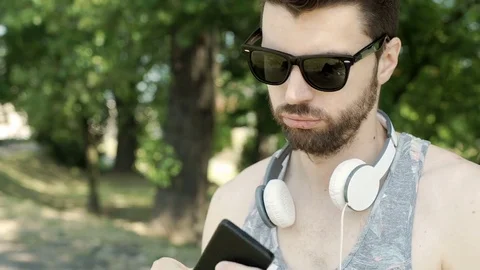 Handsome man looks irritated while waiting for someone in the park, steadycam sh Stock-Footage 78559439