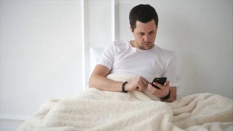 Handsome man is lying in bed with smartphone Stock Footage 81904394