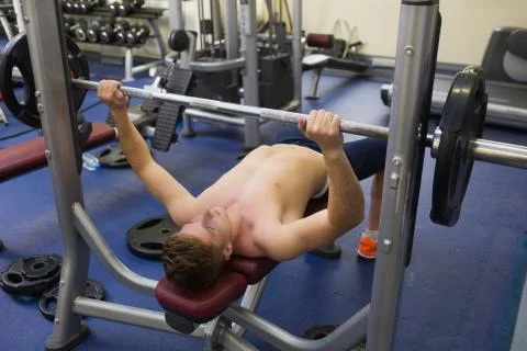 Handsome man lying on bench lifting barbell Photos