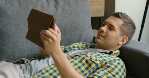 Handsome man lying on couch, browsing in tablet computer Stock Footage 113615867