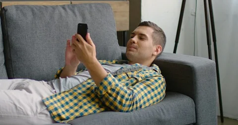Handsome man is lying on sofa, using his gadget Stock Footage 114881185