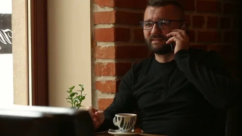 Handsome man mixing coffee in the cafe and chatting on cellphone Stock Footage 80424235
