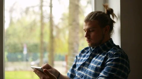 Handsome man with mud bun sitting next to the window and using tablet Stock Footage 75137859