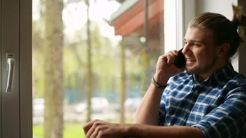Handsome man with mud bun sitting next to the window and chatting on cellphone Stock Footage 75139716