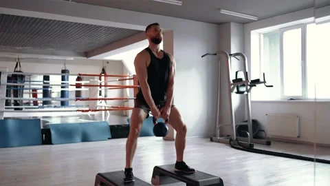 The handsome man performs knee bends with a large dumbbell with his legs Vídeo Stock 156470472