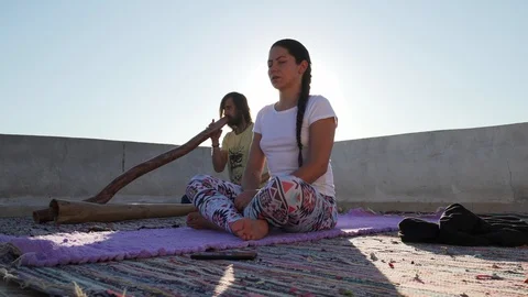 Handsome man play didgeridoo while woman practice meditation at rooftop Stock Footage 125768073
