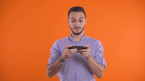 Handsome man Playing With His Smartphone And Winning On An Orange Screen Stock Footage 138519804
