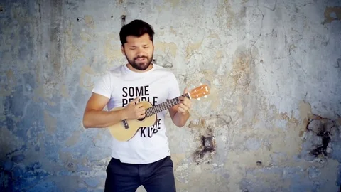 Handsome man playing ukulele small Hawaiian guitar and singing in slow motion Stock Footage 73130435