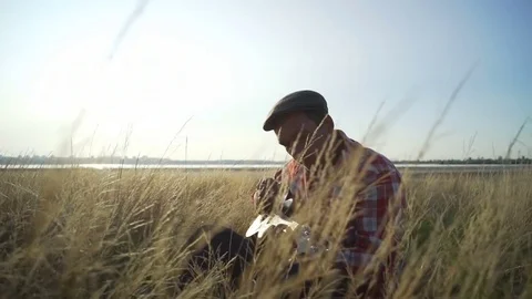 Handsome man plays guitar at wheat field sunrise rapid slow motion Stock Footage 79774013