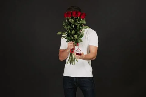 Handsome man posing on black background with gift box and red roses in hands Stock Photos