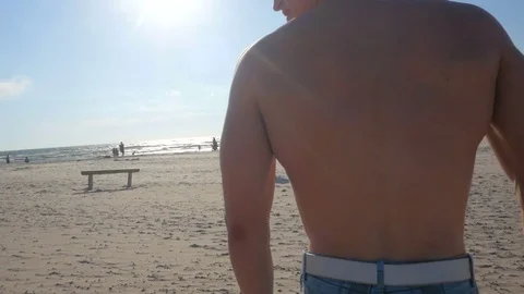Handsome man posing on a sea background, shows his back muscles. Video stock 84041796