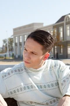 Handsome man posing in white sweater and siting on bench in town Stock Photos