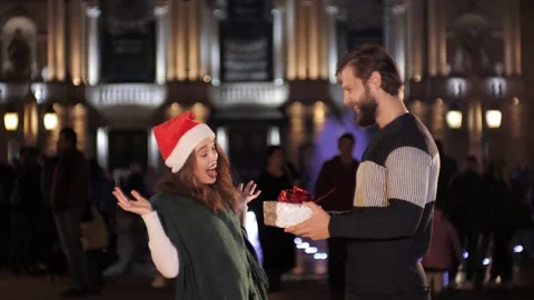 A handsome man presenting a gift girlfriend at xmas night at old town square. Video stock 142233880