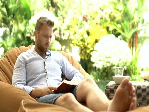 Handsome man reading interesting book while sitting on bean bag chair Stock Footage 79227093