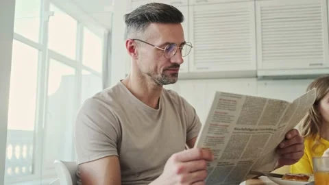 Handsome man reading a newspaper while eating breakfast at home in the kitchen Stock Footage 140797011