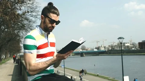 Handsome man receives message on smartphone while reading book on boulevards Stock-Footage 74420388