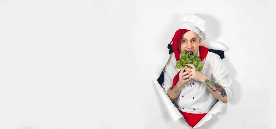 A handsome man with red dreadlocks eats lettuce leaves. Crazy cook in white a Stock Photos