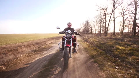 Handsome man rides a red cafe motorbike on the dirt road through the field Stock Footage 152783403