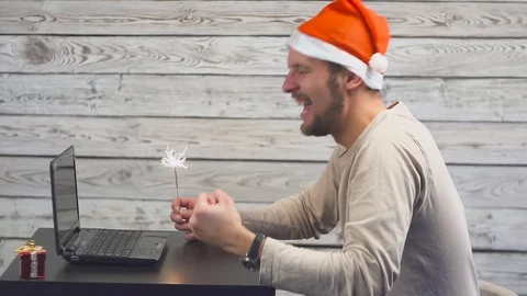 Handsome man with Santa symbol is using a laptop and rejoices with sparkler fire 스톡 동영상 105462207