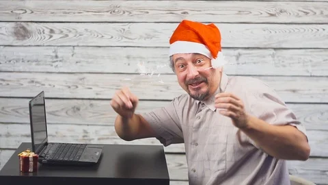 Handsome man with Santa symbol is using a laptop and rejoices with sparkler fire Видео 111750005