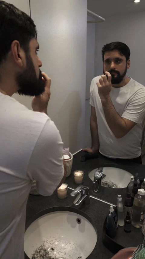Handsome man shaving thick beard with electric trimmer in bathroom Video stock 335636315