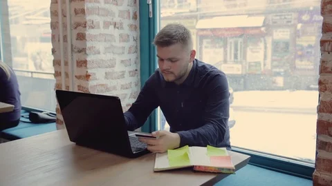A handsome man in a shirt using a laptop in a cafe holding a credit card in his Stockbeeldmateriaal 90945442