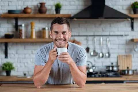 Handsome man sits at the kitchen table with cup of morning tea or coffee and  Stock Photos